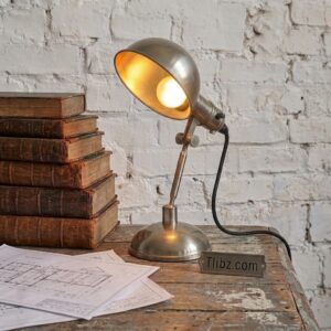 Lampe de bureau industrielle vintage éclairée posée sur table en bois avec livres anciens